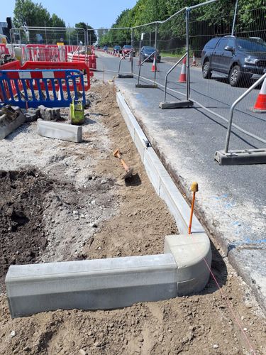 A photo of a road partially dug up and with the corner of a pavement placed in the ground. This is for the crossing island reconstruction.