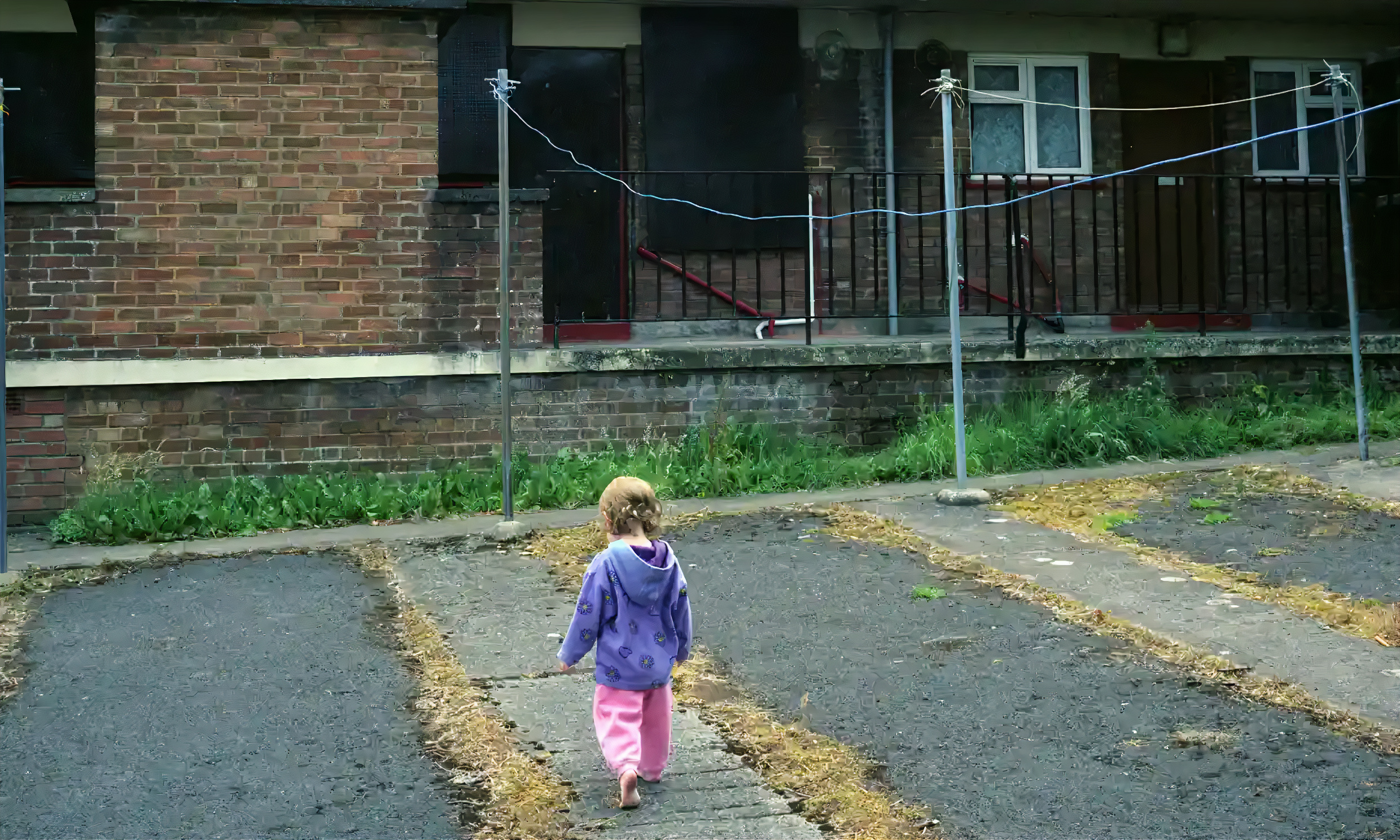 Child in purple hoodie and pink pants walks away from camera on paved path.