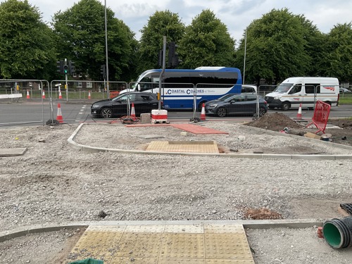 Textured paving slabs have been placed at a future crossing. The pavement and road are still gravel.