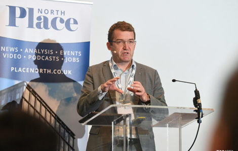 Man in a suit speaking at a podium with a "North Place" banner behind him.