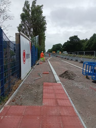 A long section of paving, most is unsurfaced and gravely. The textured paving tiles are down to mark the crossing,