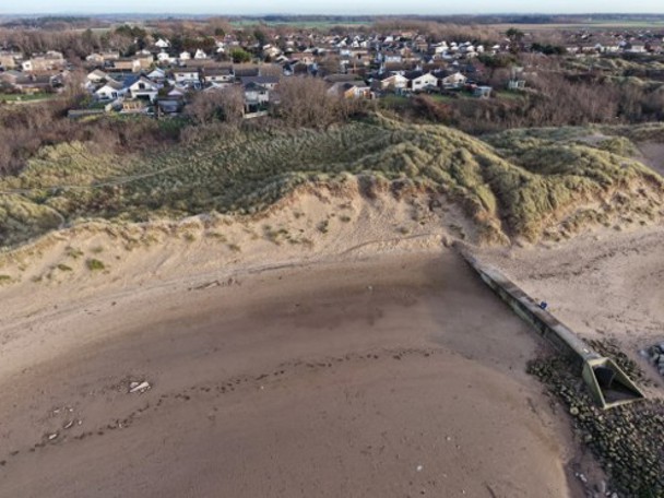 Photo of the United Utilities outfall on 16th April 2026, after Storm Dave. The darker sand on the left hand (north) side of the outfall is wet sand. This shows the water coming up further up towards the dunes than on the right hand (south) side.