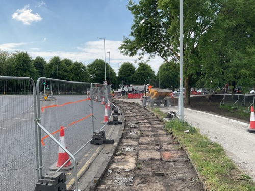 Construction works showing old paving slabs alongside the road have been lifted up, behind a line of fencing.