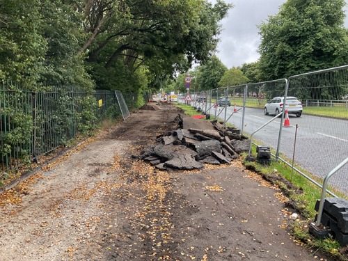 A section of pavement that is dug up, with the old surface in a pile broken up. Underneath is soil