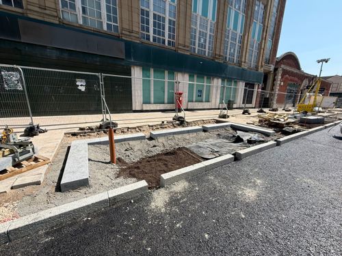 Paving kerbs outline a rectangle of a pit, for a future rain garden or tree on the pavement part of the road.