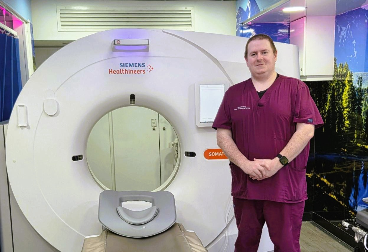 CAT scanner with health service  employee standing next to it.