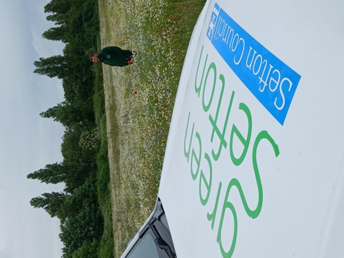 Joe Kennedy standing in a wildflower meadow. A vehicle is in the foreground with the words 'Green Sefton' printed on its hood.