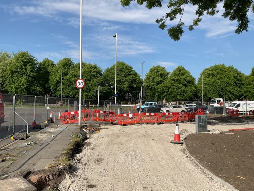 A wide gravel pavement with orange barriers at the end, behind fencing at a junction.