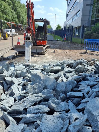 Heavy machinery has broken up the old pavement by Atlantic park Drive. There is lots of large broken grey paving in rubble piles.