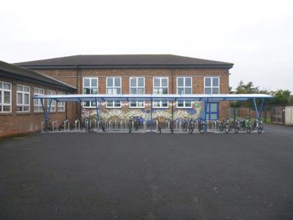 An image of a bike shelter, it is blue with a large plastic roof and space for around 40 bikes.