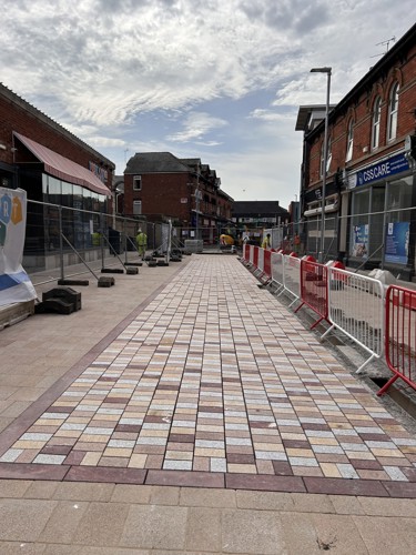 A photo on Market Street showing the new paving slabs on the new pedestrianised part of the work. They are different shades of red. Fencing is still up on both sides of the street.