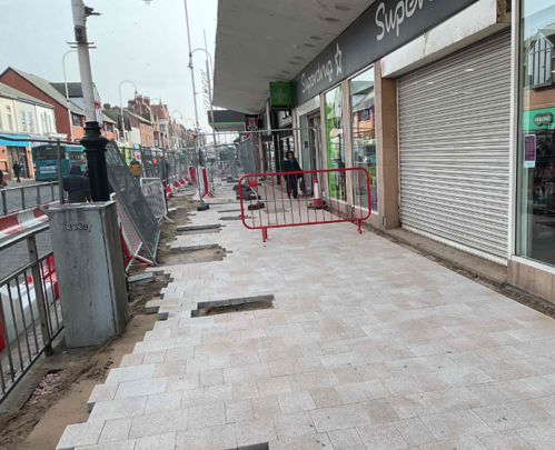 A progress picture of Eastbank Street, there are new paving tiles outside superdrug. There is a red fence. - February 2025